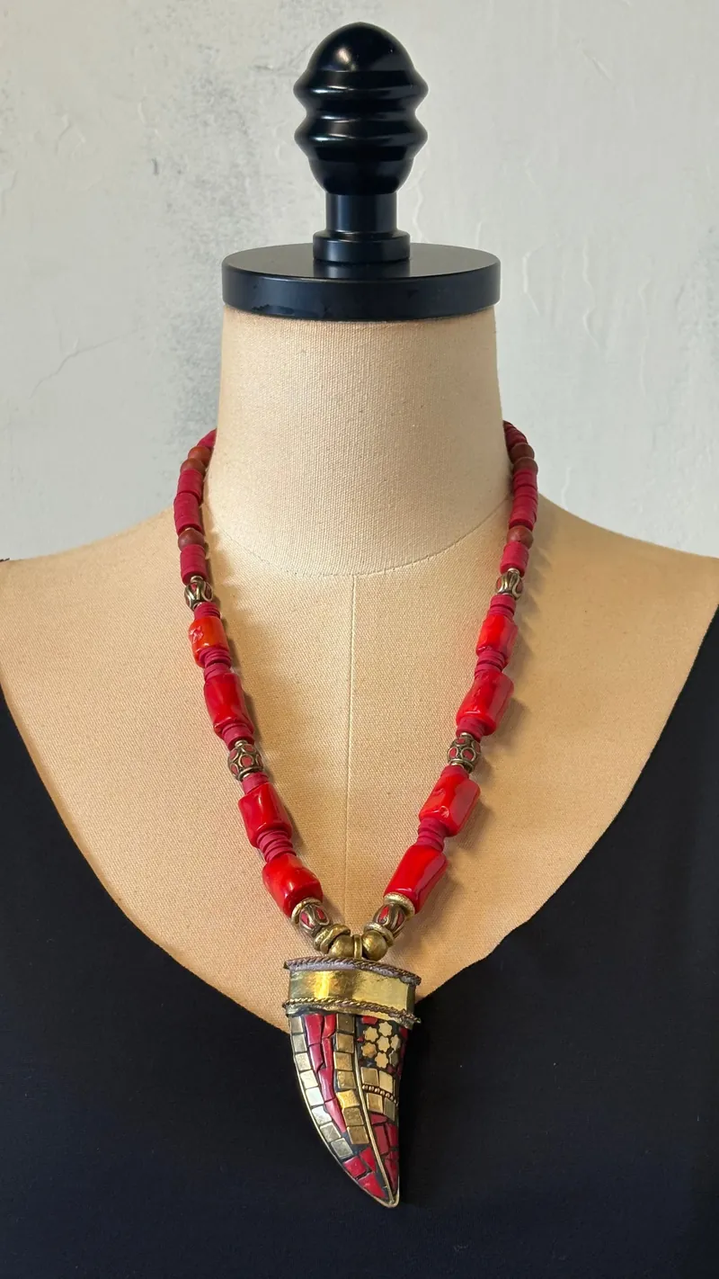 A red coral and brass horn necklace by Mya Lambrecht on a dress form, from the Gaia Pre-Loved collection
